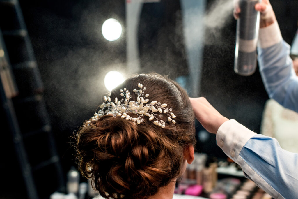 cropped shot of hairstylist fixating clients hairdo with hair spray
