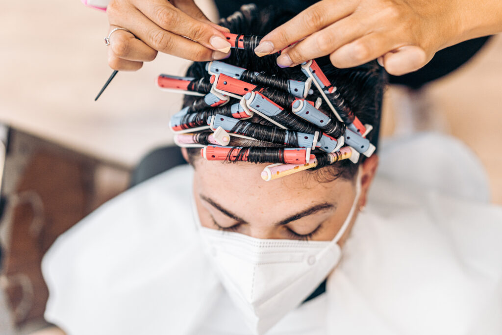 Profile of a blonde hairdresser arranging the curls of the hair of a man indoors